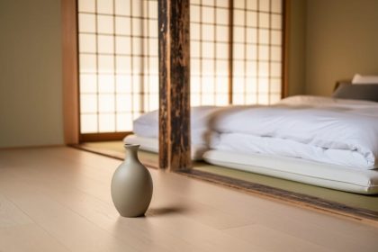 Japanese-inspired minimalist living room with a low platform bed, shoji-style screen filtering light, and a single ceramic vase on a light wood floor.