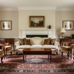 Symmetrical traditional living room with crown molding, warm wood furniture, a Persian rug, and upholstered seating facing a fireplace under soft natural light.